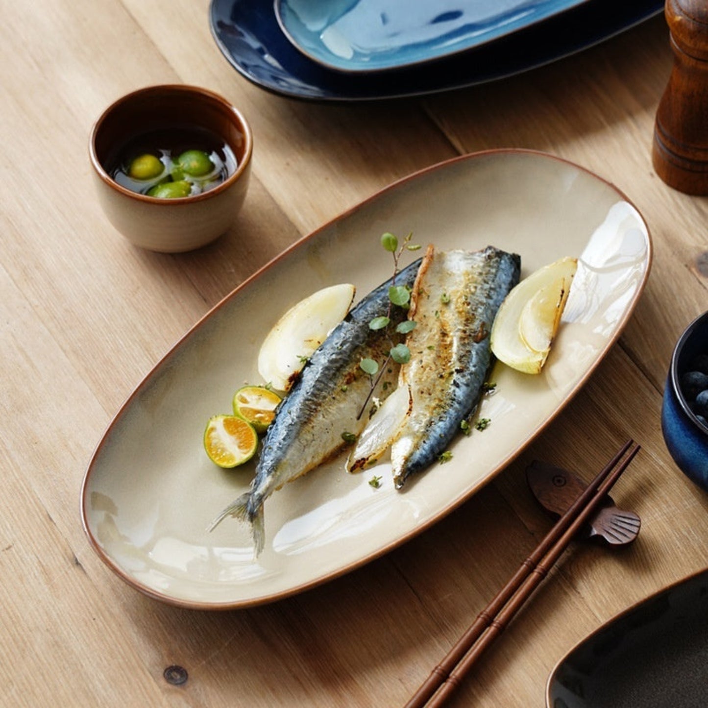 High-quality beige ceramic plate with fish dish, garnishes on a wooden table with chopsticks and a small bowl.