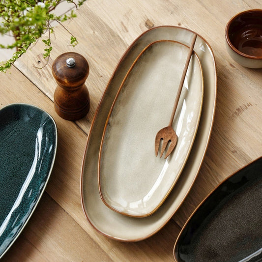 High-quality beige ceramic platters on a wooden surface with a wooden fork and salt grinder. Ceramic platters in black, blue and beige. 