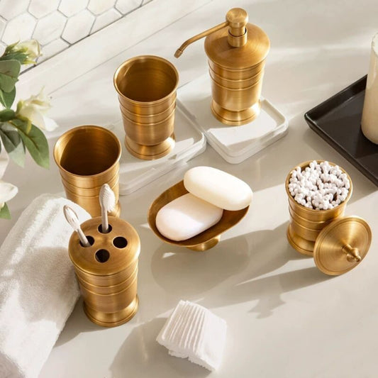 Gold bathroom accessory set including cups, dispenser, and soap dish on a white surface and a flower on the left. 