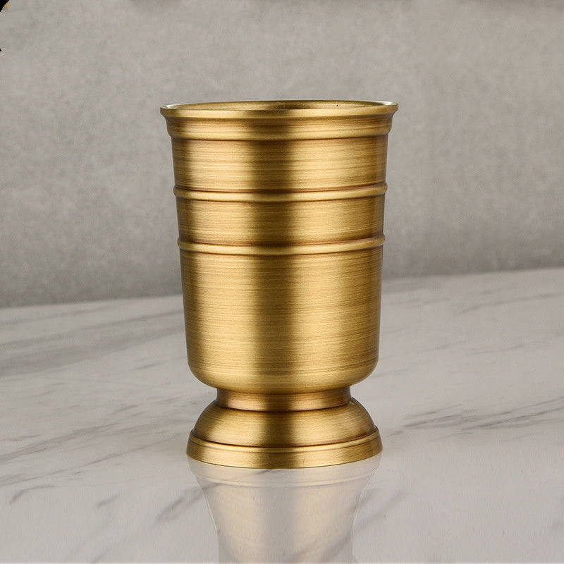 A set of gold-colored copper bathroom accessories including a toothbrush holder, soap dispenser, tumbler, and a tray, displayed on a white surface. Stylish golden bathroom decor designed to elevate every bathroom space. 