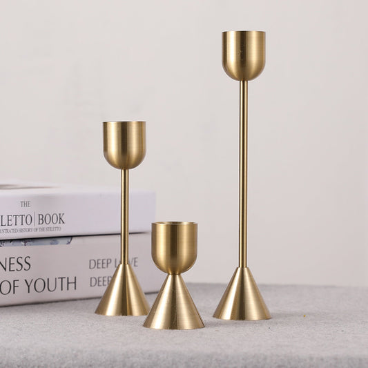 Set of three gold candle holders on a white background and a light fabric surface. Two books in the background. Minimalist home decor. Timeless design. Modern home decor.  
