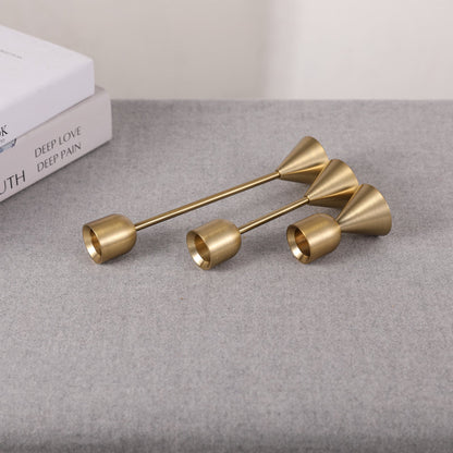 Set of three gold candle holders with different sizes on a grey surface and a white background. Two books in the picture. Minimalist home decor. Timeless design. Modern home decor.  