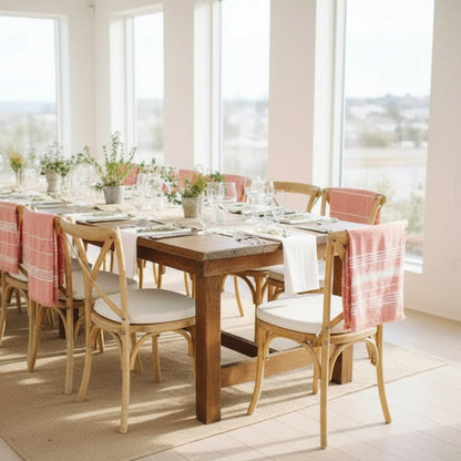 Dining room with wooden table and chairs, pink tablecloths, and large windows. Jute table runner on a wooden table. Natural decor styling idea for calm and modern design. 