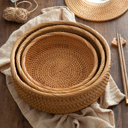 Set of handmade rattan woven storage baskets on a wooden surface with a beige cloth and wooden sticks. Earthy and natural kitchen and living room decor. 