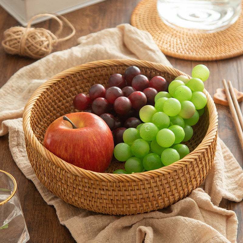 A handmade rattan woven storage baskets with fruits on a wooden surface with a beige cloth and wooden sticks. Earthy and natural kitchen and living room decor. 
