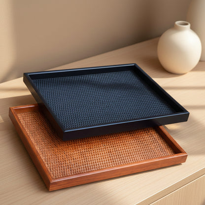 Two handmade, one black and one brown, rectangular wooden rattan tray on a wooden surface with soft shadows and a beige wall in the background. Warm and earthy home ambience.