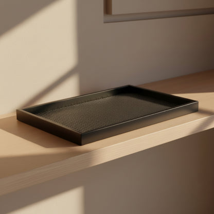 Handmade black rectangular wooden rattan tray on a wooden surface with soft shadows and a beige wall in the background. Warm and earthy home ambience. 