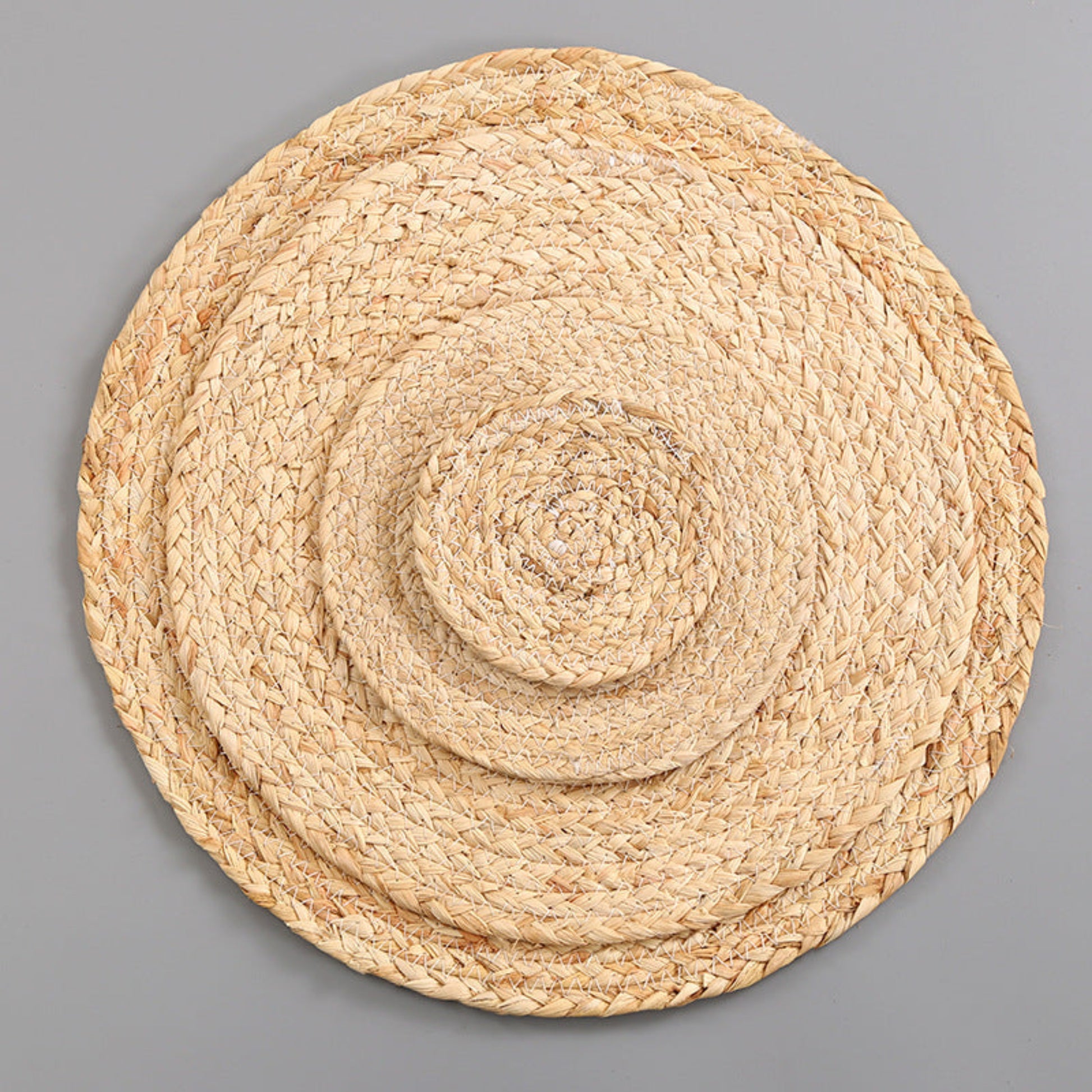 Beige round woven mat in different sizes on a gray background. Handmade natural decor for calm and modern tables. Minimalist and earthy pieces. 