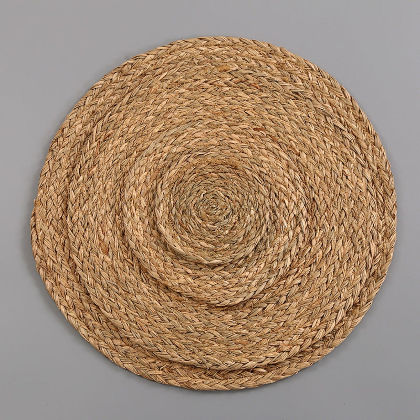 Brown round woven mat in different sizes on a gray background. Handmade natural decor for calm and modern tables. Minimalist and earthy pieces. 