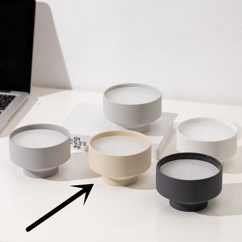 Set of five ceramic bowls in different colors on a white surface on a white wall background. Laptop in the picture. Scandinavian decor simplicity. Minimalist handmade scented candles. Beige candle is in the center. 