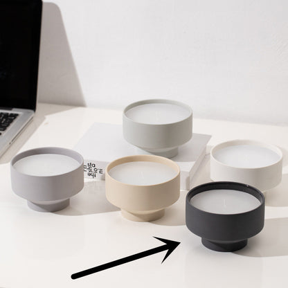 Set of five ceramic bowls in different colors on a white surface on a white wall background. Laptop in the picture. Scandinavian decor simplicity. Minimalist handmade scented candles. Black candle is in the center. 
