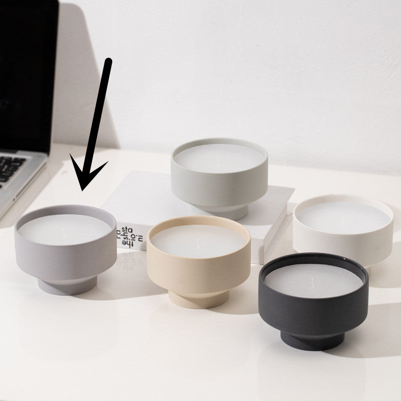 Set of five ceramic bowls in different colors on a white surface on a white wall background. Laptop in the picture. Scandinavian decor simplicity. Minimalist handmade scented candles. Grey candle is in the center. 