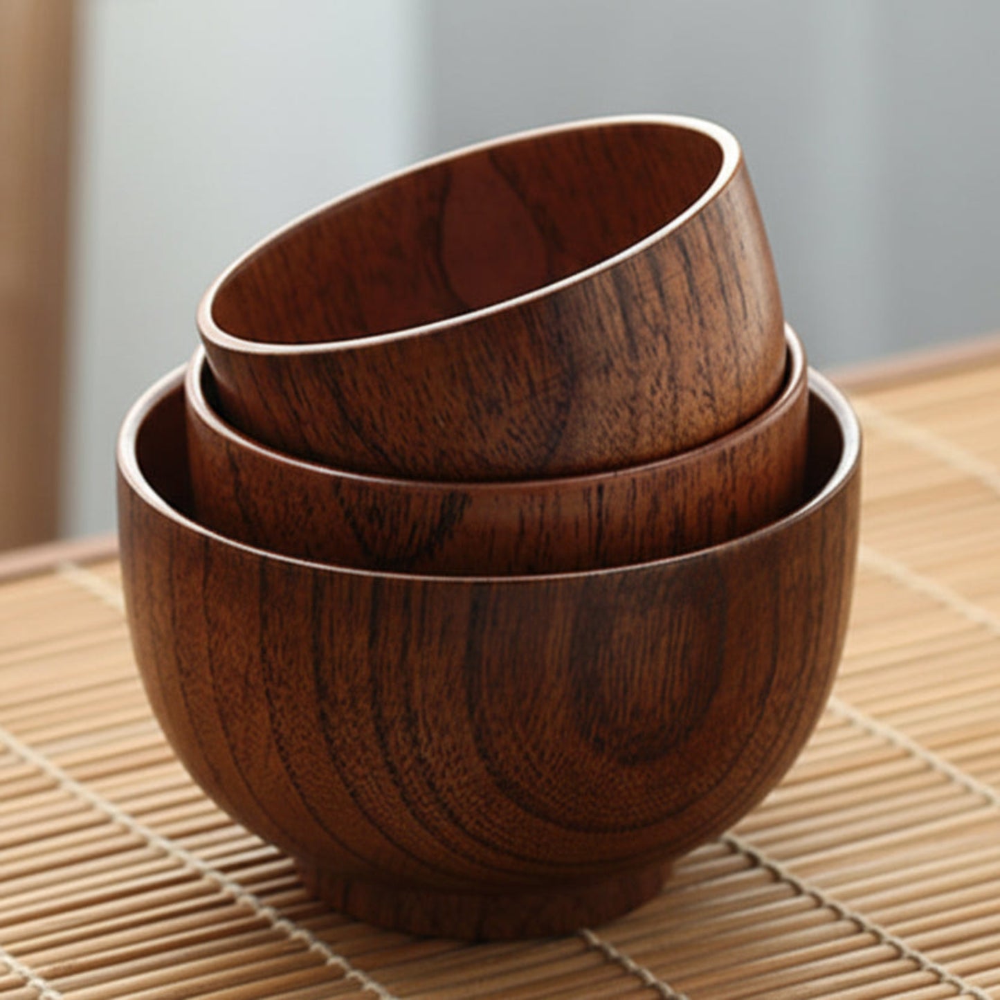 Set of three wooden bowls stacked on a bamboo mat. Solid wood. Japanese style. Earthy and natural. 