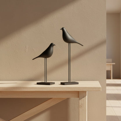 Two black bird sculptures on stands against a beige wall background. Two bird-shaped decor items on a wooden surface with a beige wall background. Natural and warm ambience. 