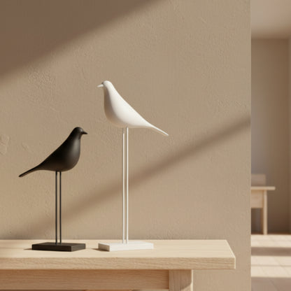 Two bird-shaped decor items, one black and one white, on a wooden surface with a beige wall background. Natural and warm ambience. 