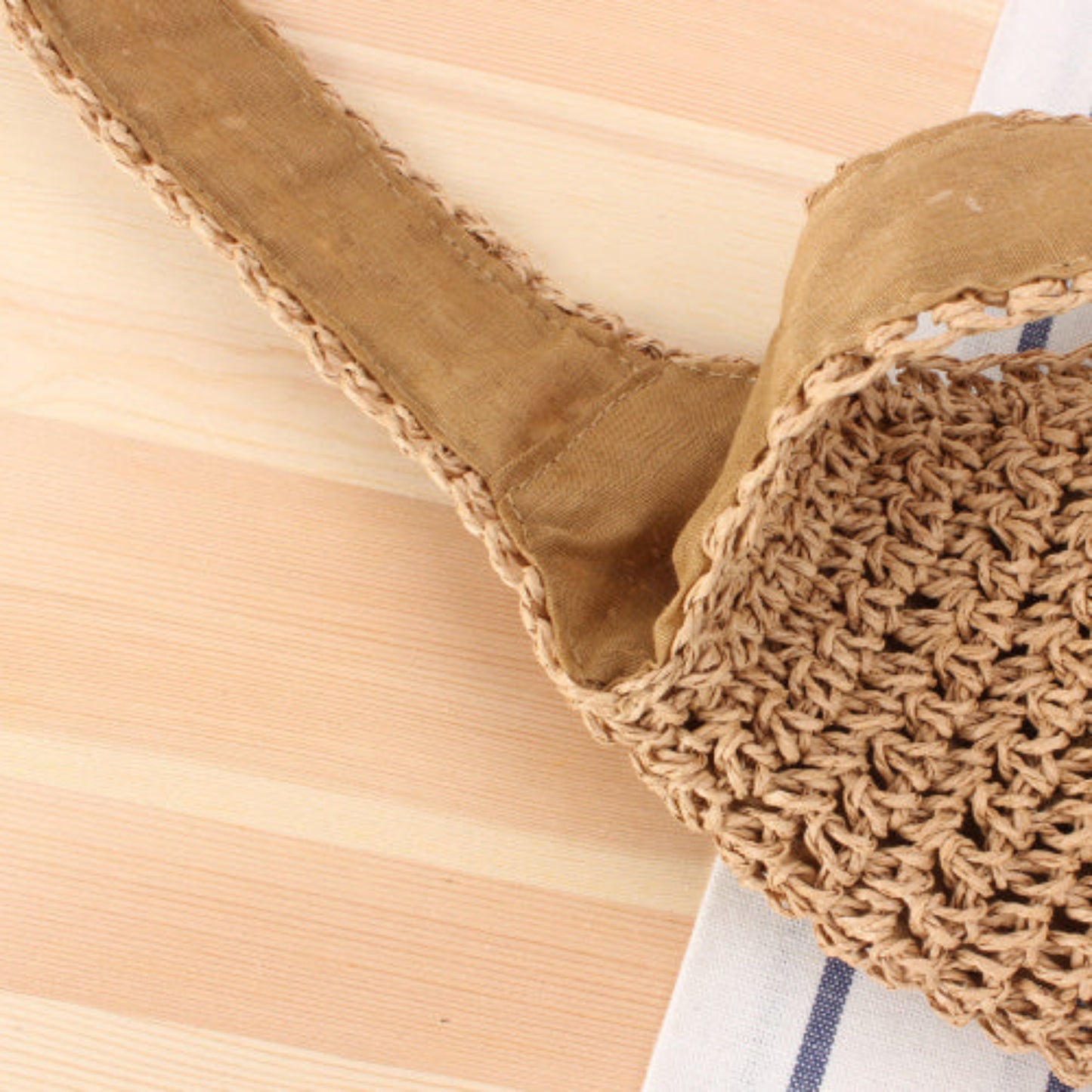 Close-up of a straw woven brown bag on a wooden surface. Warm and earthy design with white blue fabric in the background. 