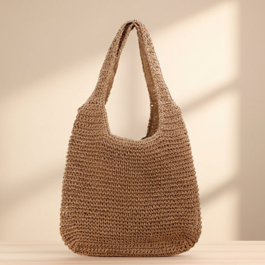 Brown straw woven handbag on a wooden surface with a beige background. 