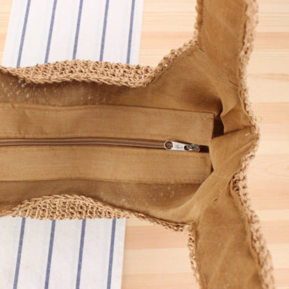 Brown straw woven bag with a close up from the zipper on a wooden surface and on white-blue fabric.  