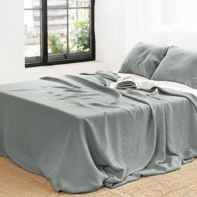 Gray plain linen bedspread on a bed in a bright room with a window. Bed with gray plain linen bed sheet and pillows in a bedroom. Earthy and natural home and bed decoration. 