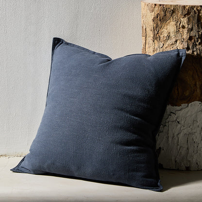 A blue pure cotton and linen pillow on a earthy and warm surface with a plain wall and wood in the background.
