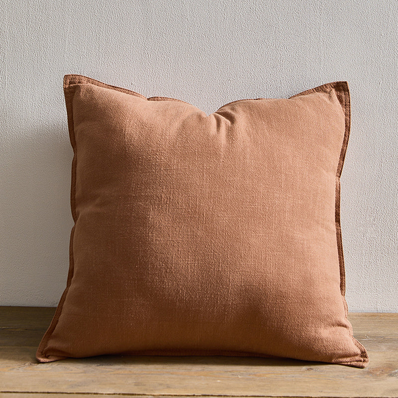 A brown pure cotton and linen pillow on a wooden surface with a plain white wall in the background. Warm and natural ambience. 