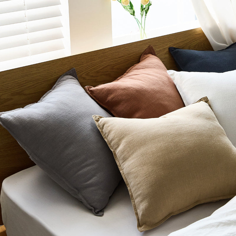 Five colorful pure linen pillows on a bed with a wooden headboard and window in the background. wooden and natural ambience. Five pillows on a white bed sheet. 