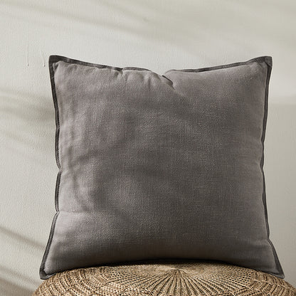 A grey pure cotton and linen pillow on a natural surface with a plain white wall in the background. Warm and natural ambience. 