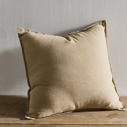 A beige pure cotton and linen pillow on a wooden surface with a plain white wall in the background. Warm and natural ambience. 