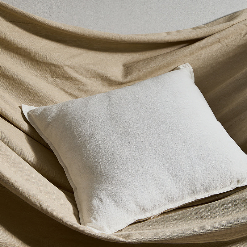 A bright pure cotton and linen pillow on a fabric surface with a plain wall in the background. Warm and natural ambience. 