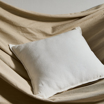 A bright pure cotton and linen pillow on a fabric surface with a plain wall in the background. Warm and natural ambience. 