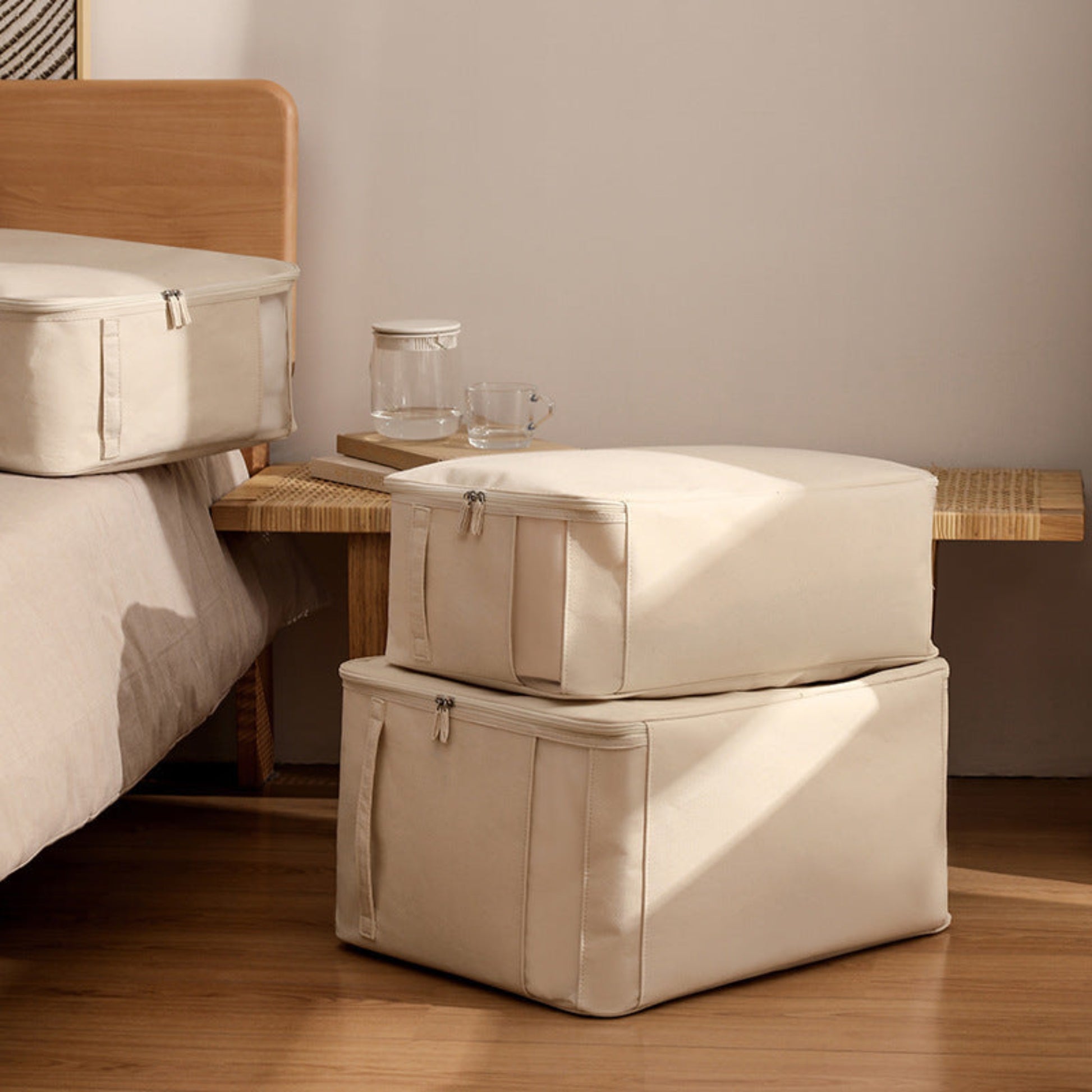 Two beige storage boxes stacked on a wooden floor with a bed and bench in the background. On beige storage box ist on the bed. 