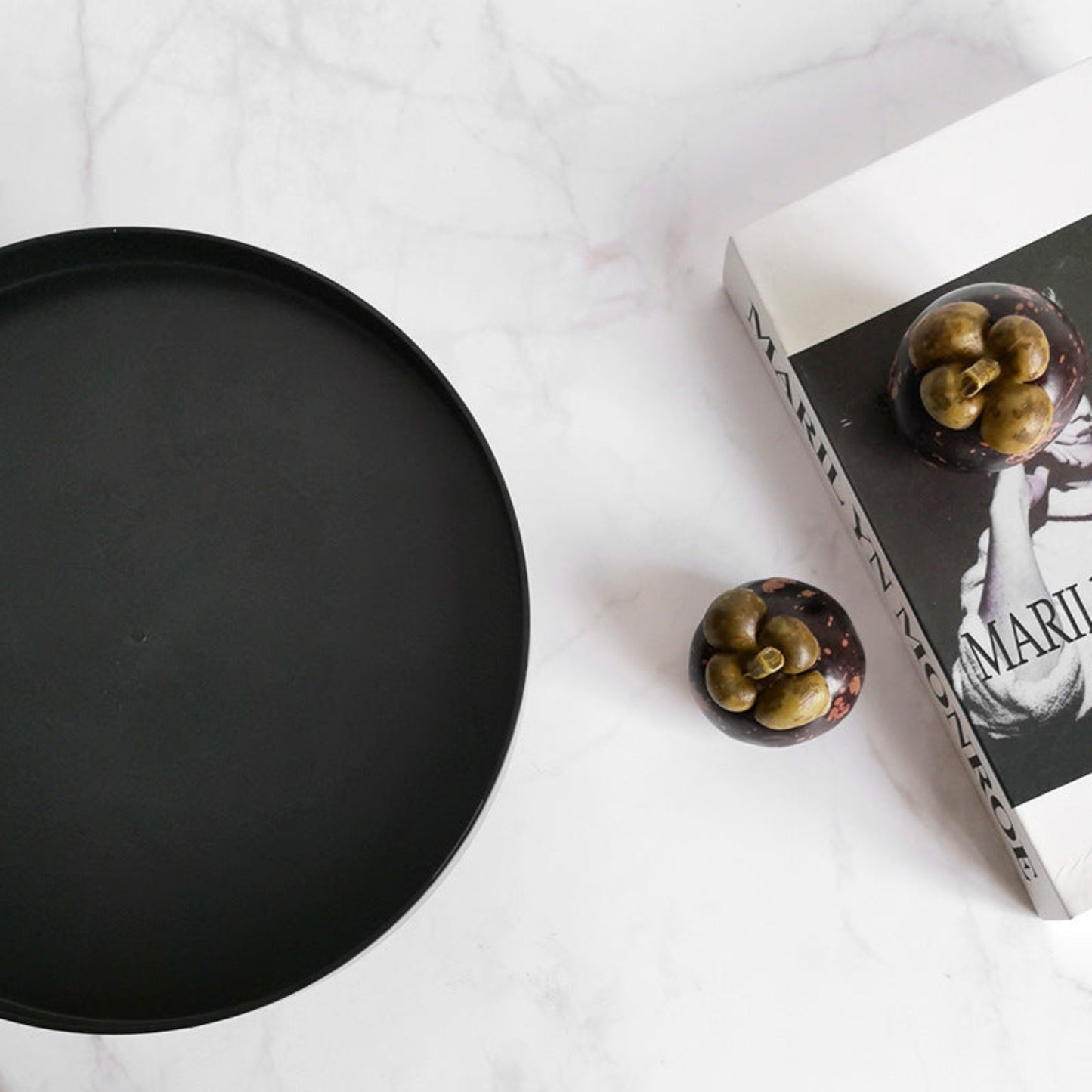 Black round tray on a white surface with a book and decorative item. Minimalist home decor. Timeless and minimalist design. 