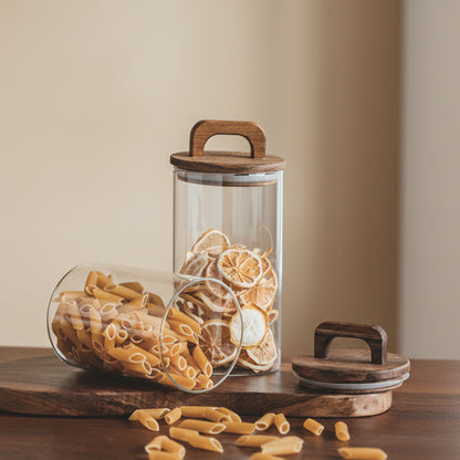 Glass jars with wooden lids containing pasta and dried lemons on a wooden surface against a beige wall background. Acacia wood sealed storage tank. Earthy and warm kitchen and home decor. 