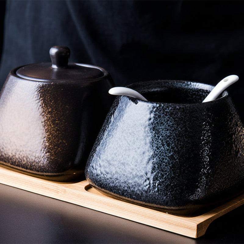 Two dark ceramic pots with wooden bases on a dark background. black and brown ceramic spice jar. Modern accessories, natural materials, and timeless kitchen piece. 