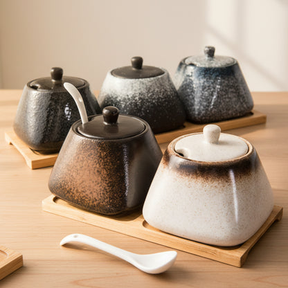 Set of different colors ceramic pots with lids and a spoon on a brown wooden tray and on a wooden table surface. Modern accessories, natural materials, and timeless kitchen piece. 