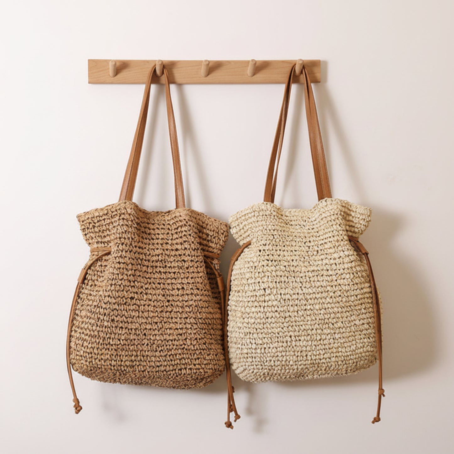 Two woven bags with brown handles hanging on a wooden hook against a white wall. Natural chic look. Natural decor styling. Natural accessories. 