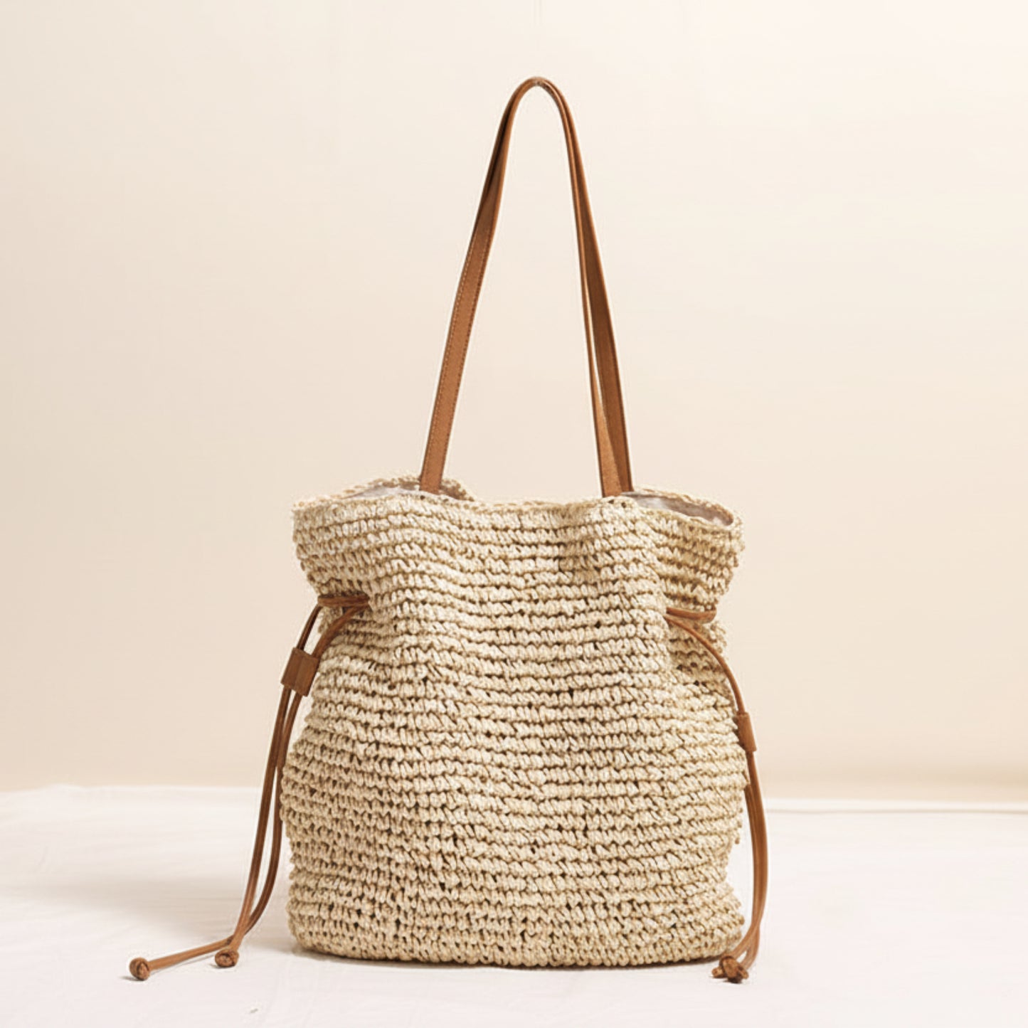 Woven beige straw bag with brown straps on a light beige background and a white surface. Natural chic look. Natural decor styling. Natural accessories. 