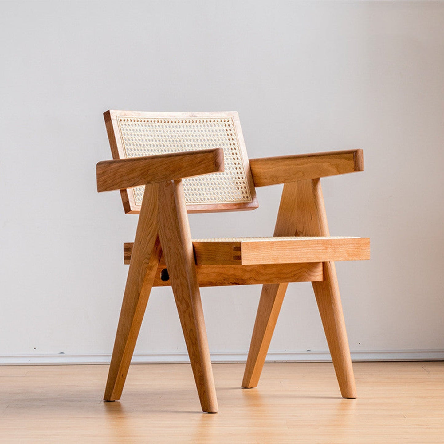 Wooden chair with woven backrest on a white wall background and a wooden floor. Warm and beige ambience. 