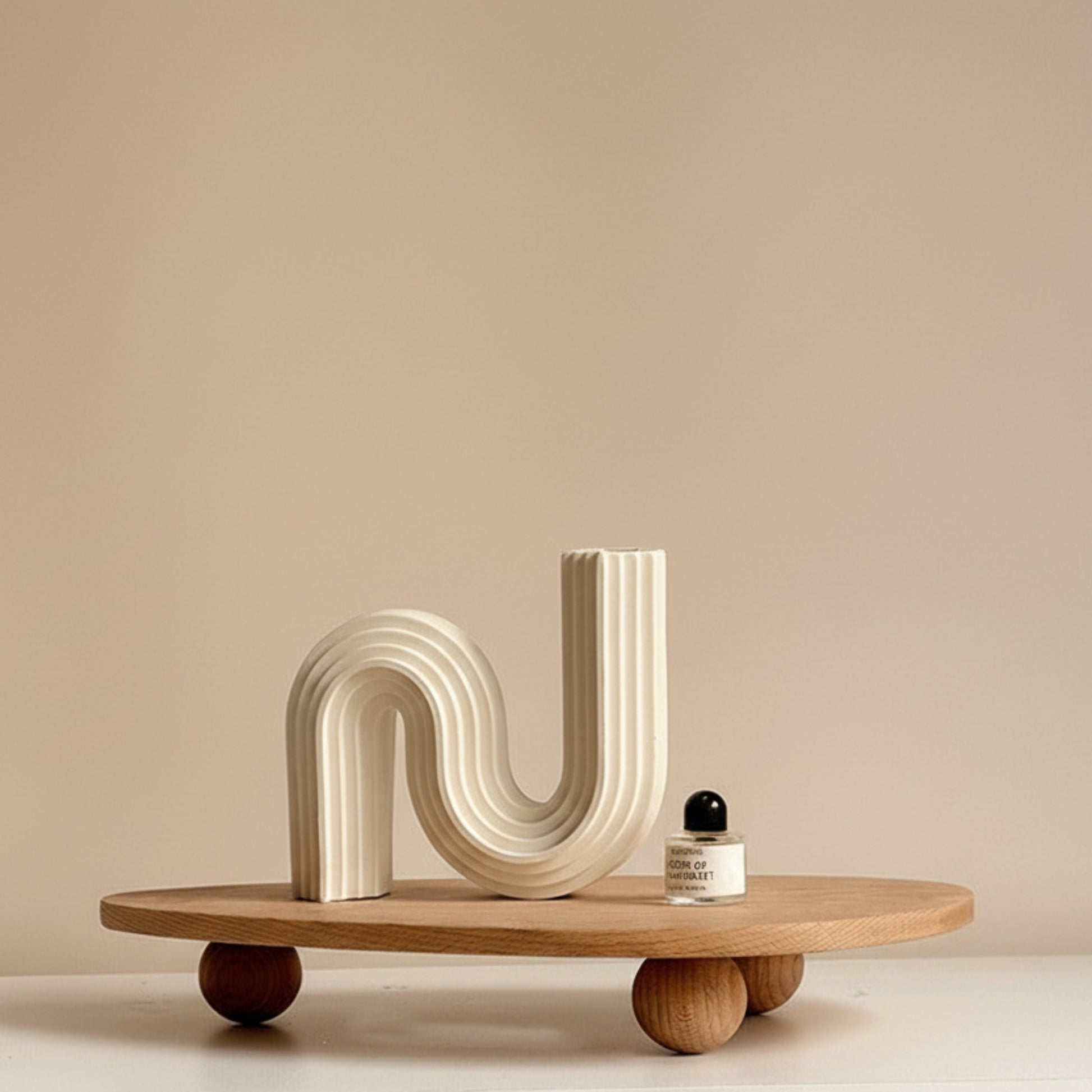 Wooden tray with unique ball high foot design on a white-beige surface and against a white beige wall. Natural and earthy decor item with a irregular triangle shape that holds a parfume and another decor item. 