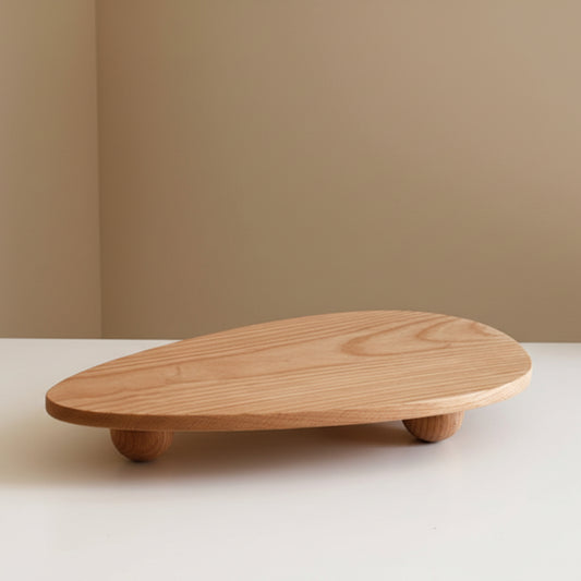 Wooden tray with unique ball high foot design on a white surface and a beige wall. Natural and earthy decor item with a irregular triangle shape. 