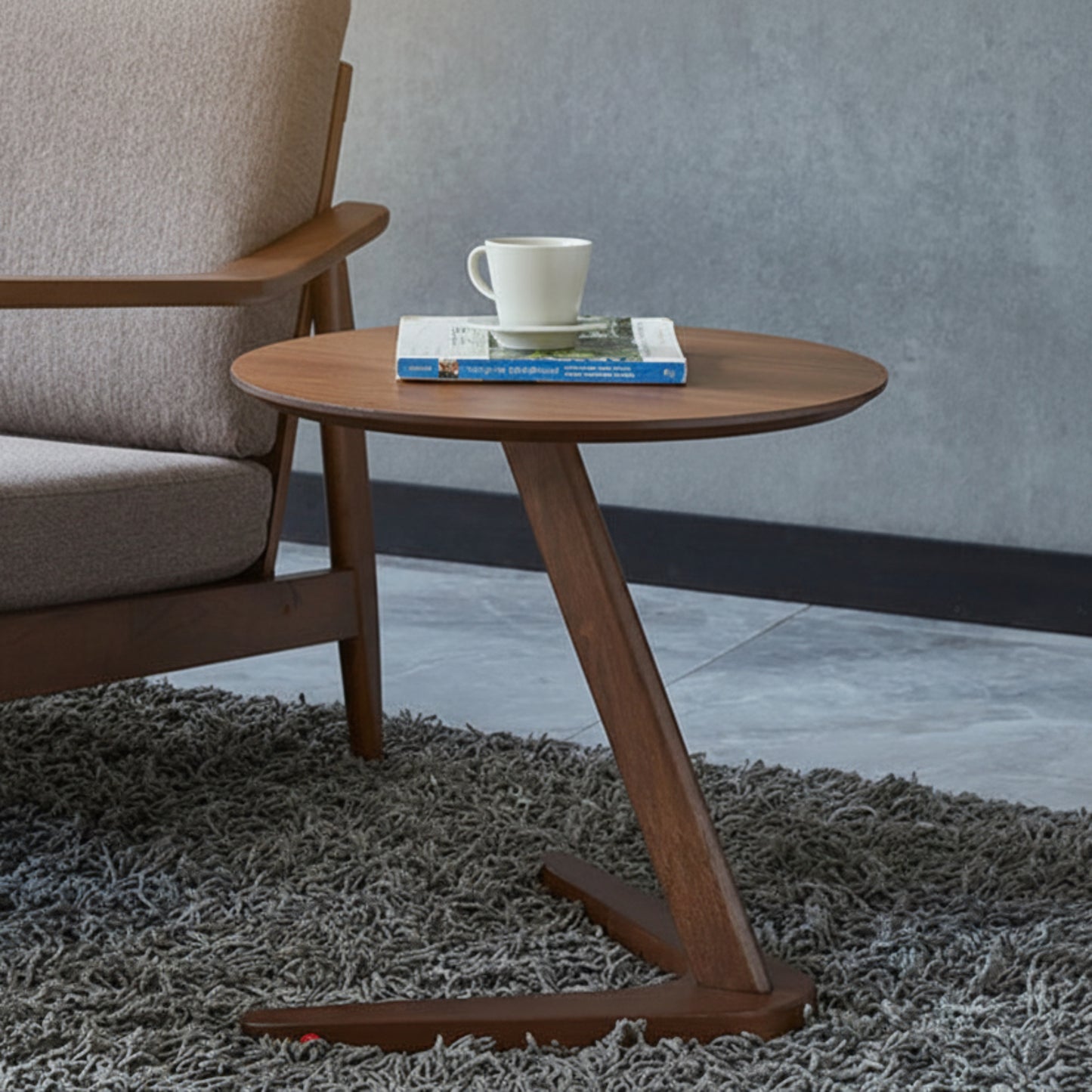 Wooden side table with a cup and book next to a gray armchair on a textured rug. Grey wall background. Minimalist nordic design. 