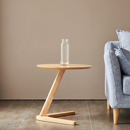 Wooden side table with a clear vase against a beige wall, next to a blue-gray sofa. Minimalist and natural side table. 