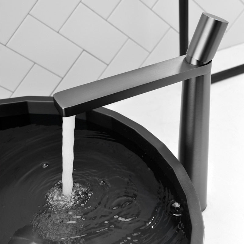 A grey colored basin faucet with a sleek design, displayed against a white background.  Running water out of the basin faucet. Minimalist bathroom or kitchen faucet with premium copper faucet. Timeless design for warm and modern interiors.