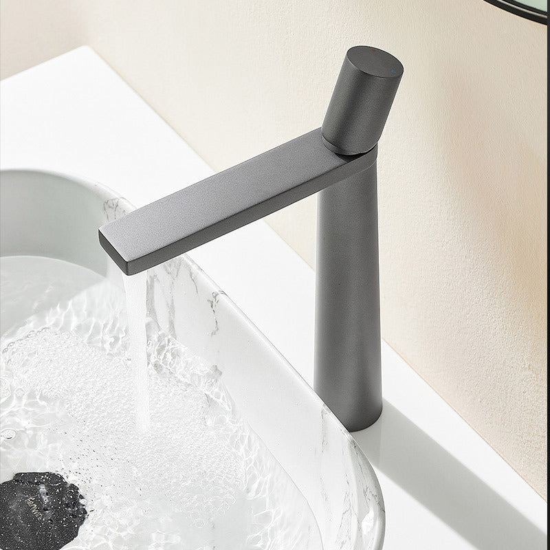 A grey colored basin faucet with a sleek design, displayed against a beige/white background and running water.  Minimalist bathroom or kitchen faucet with premium copper faucet. Timeless design for warm and modern interiors.