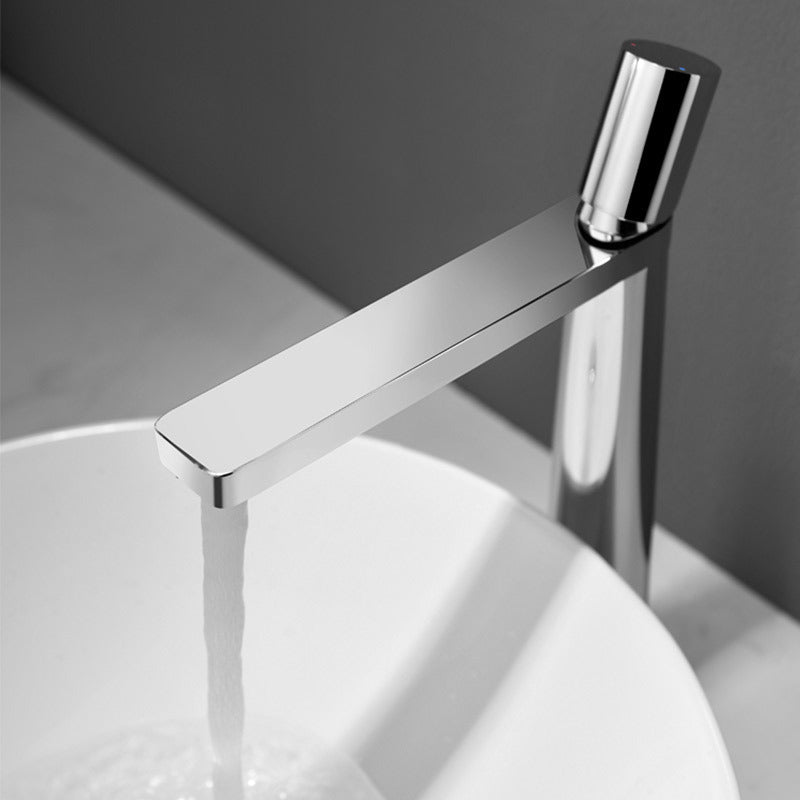 A silver colored basin faucet with a sleek design, displayed against a dark background and running water.  Minimalist bathroom or kitchen faucet with premium copper faucet. Timeless design for warm and modern interiors.