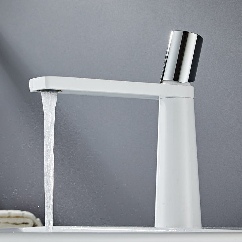 A white colored basin faucet with a sleek design, displayed against a grey background and running water.  Minimalist bathroom or kitchen faucet with premium copper faucet. Timeless design for warm and modern interiors.