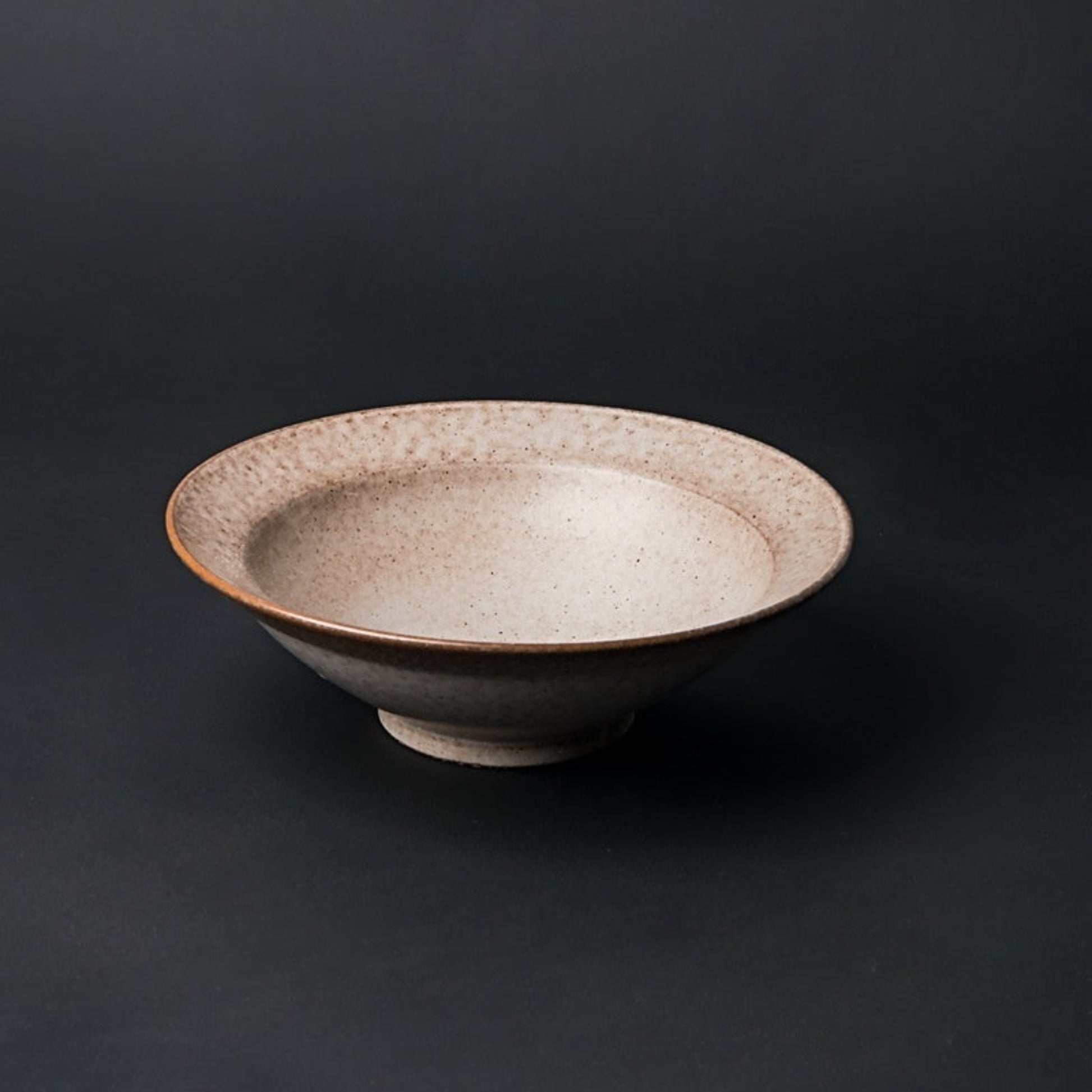 Ceramic bowl with speckled texture on a dark background. beige ceramic bowl on a dark surface. Natural textures and earthy, warm tones. Timeless minimalist and warm design.  