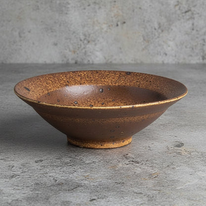Brown ceramic bowl on a grey surface with a grey blurry background. Natural textures and earthy, warm tones. Timeless minimalist design.  