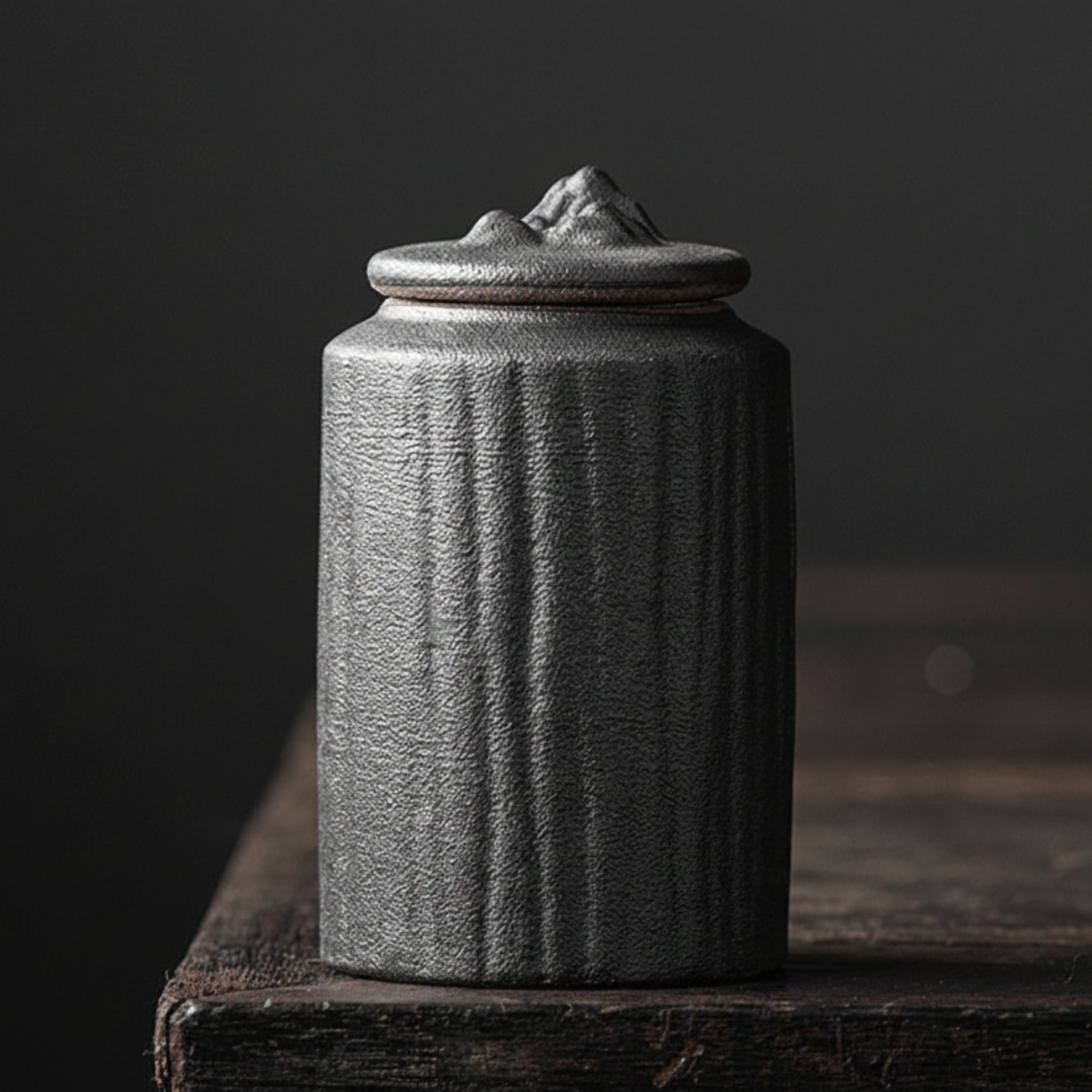 Zen style pottery black-Guanshan cylindrical tea can on a dark background. black and hand trimmed ceramic jar with lid on a dark wooden surface, with a dark background. Stylish kitchen decor. Modern and traditional. Timeless piece.