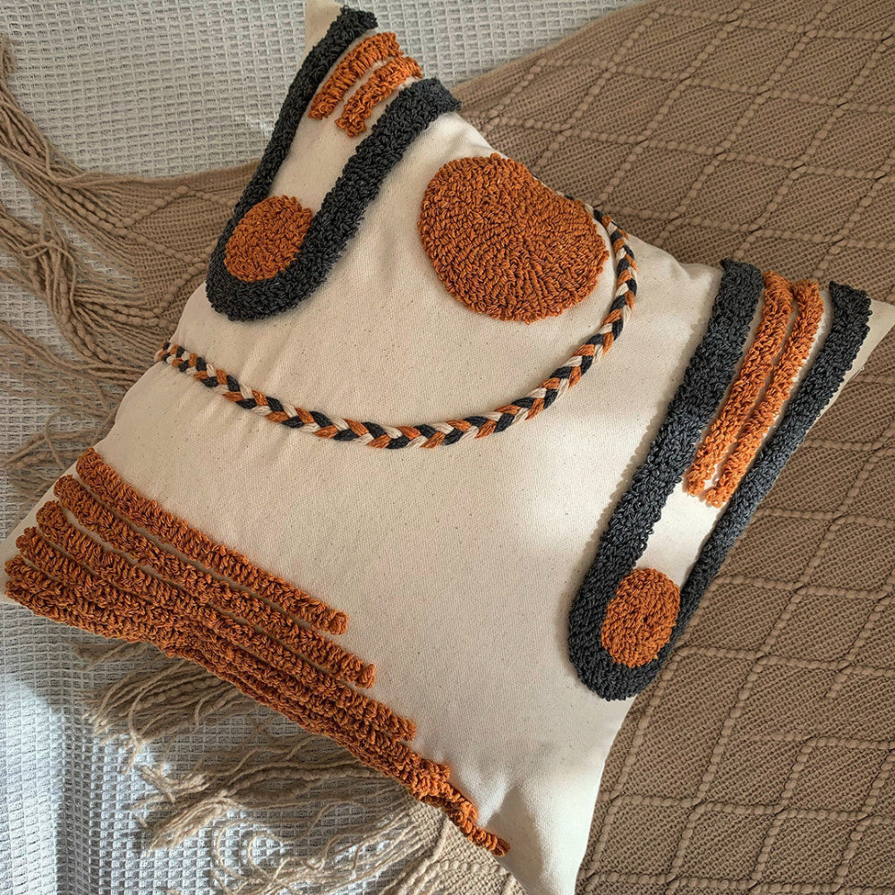 Beige, black and orange textured pillow on a blanket with tassels and on a white fabric textured surface. Scandinavian interior with warm light.  